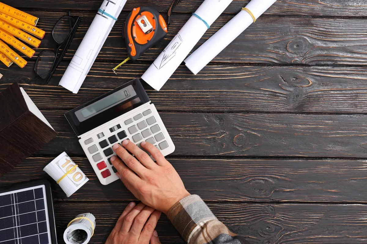 Mains posées sur une calculatrice au milieu de plans roulés, d'un mètre ruban et de crayons sur une table en bois
